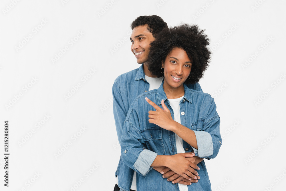 Smiling young african american couple two friends man woman in denim casual clothes posing hugging pointing finger at copy space looking camera isolated on white color wall background studio portrait Smiling young african american couple two friends man woman in denim casual clothes posing hugging pointing finger at copy space looking camera isolated on white color wall background studio portrait