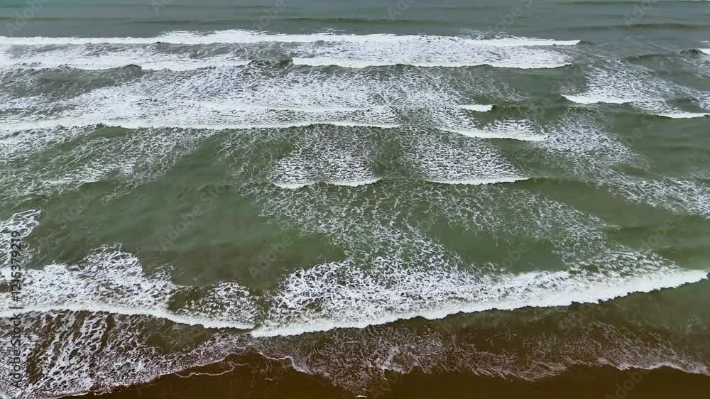 Static drone shot of the ocean with calm waves reaching the shore of a white sand beach on a tropical island of Pakistan during bright sunny day