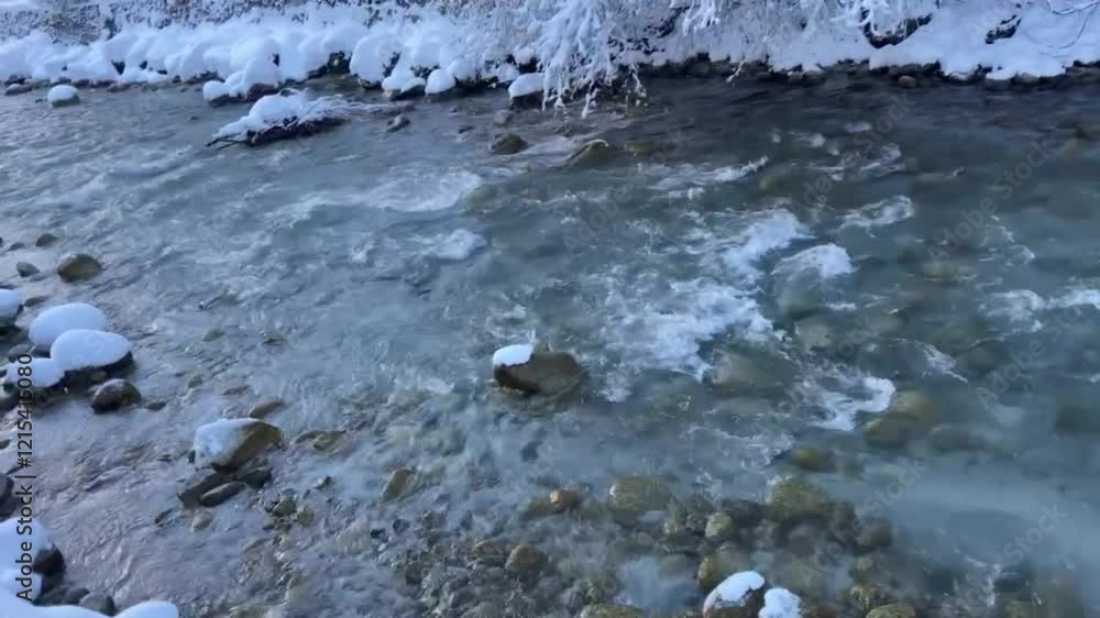 Mountain river. Crystal-clear mountain stream flowing swiftly through a snowy winter forest on a sunny day. Snowdrifts and tree branches covered in sparkling snow create a serene, natural wonder. Mountain river. Crystal-clear mountain stream flowing swiftly through a snowy winter forest on a sunny day. Snowdrifts and tree branches covered in sparkling snow create a serene, natural wonder.