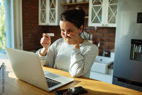 Woman showing positive pregnancy test to laptop in modern kitchen photo