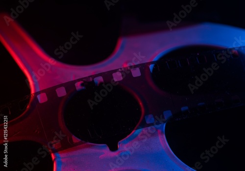 Close-up of a filmstrip with cinematic reel illuminated by vibrant red and blue neon lighting, creating a moody artistic composition highlighting vintage photography and analog film culture photo