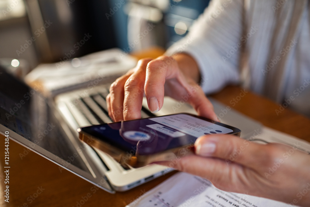 Senior woman using smartphone for online banking next to laptop at home Senior woman using smartphone for online banking next to laptop at home