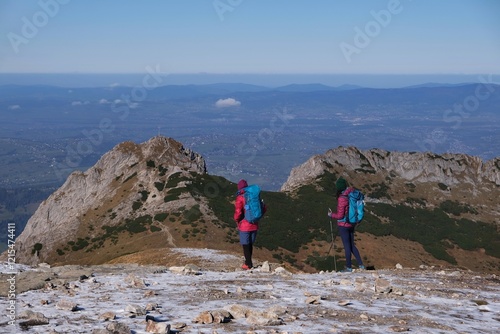 Scenery of autumn Tatras Mountains with two silhouettes of hiking girls. Giewont Peak on background. Czerwone Wierchy range from around Kasprowy Wierch Peak, Tatras Mountains, Poland.  