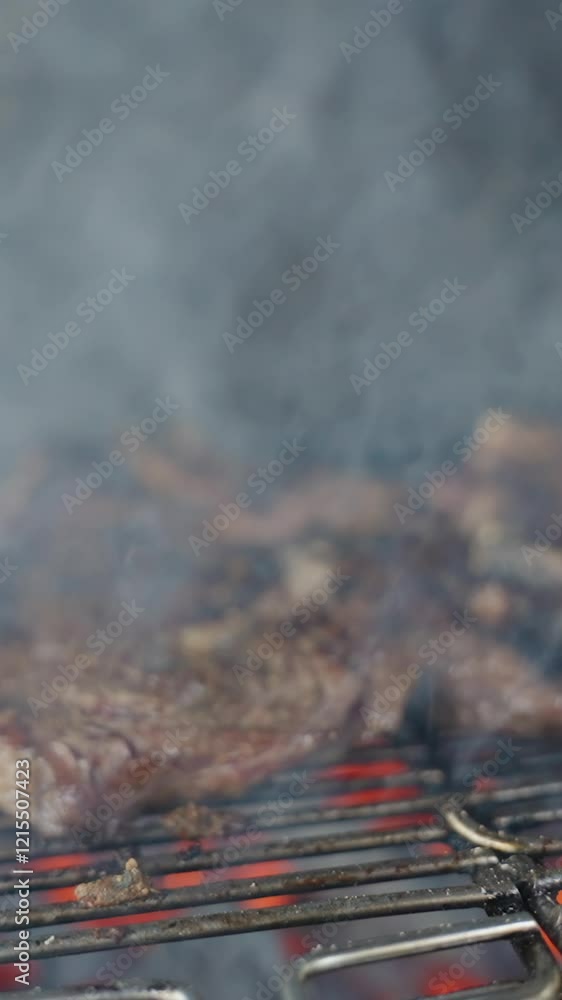 Vertical video. Slow motion Steaks Cooking on a Grill Surrounded by Smoke and Flames Highlighting Their Charred Texture and Sizzling Appearance Outdoor Barbecue