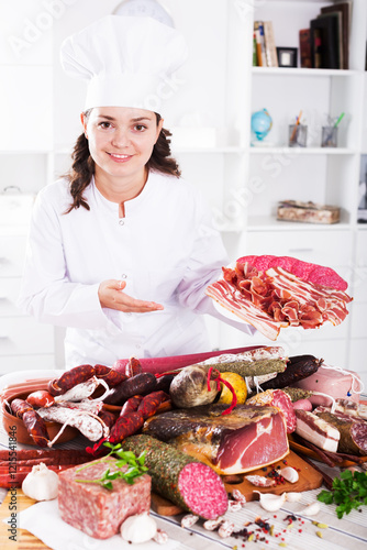 Cook costs near table with smoked products and sausage and holds in hand plate with jamon photo