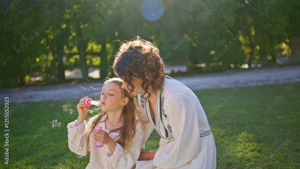 Happy family blowing soap bubbles sitting on green grass in sunny park closeup Happy family blowing soap bubbles sitting on green grass in sunny park closeup