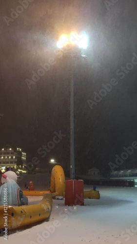 A snowstorm at night in a mountain ski resort. The wind blows and snow falls, visible on a streetlamp.