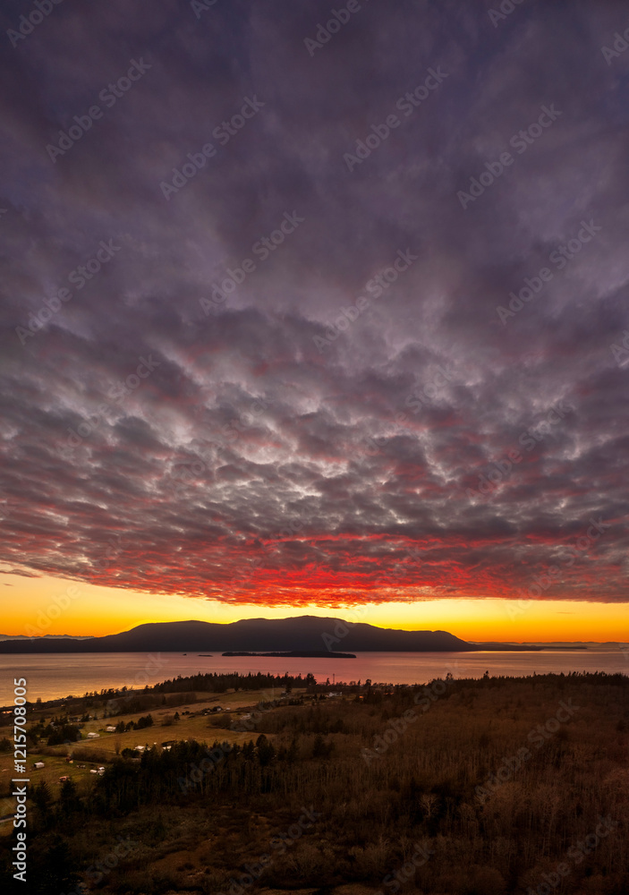 Obraz premium Dramatic and colorful sunset over Orcas Island in the San Juan Islands archipelago of Washington State. Aerial drone view of an amazing cloudscape as seen from Lummi Island located in the Salish Sea.