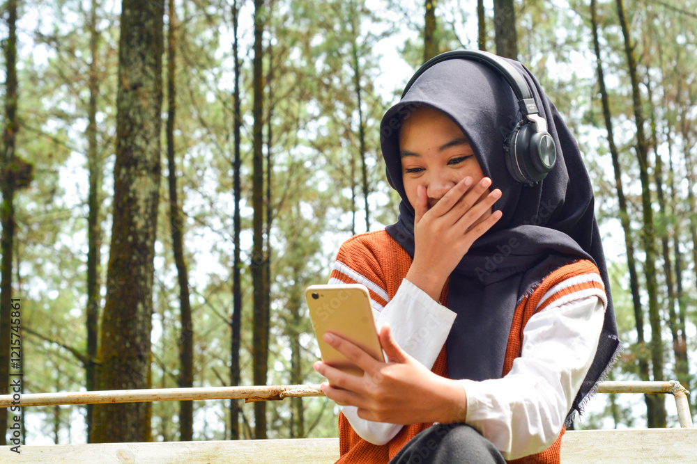Naklejka premium Beautiful woman asian muslim standing in front of a fresh forest park with smart phone and headphones