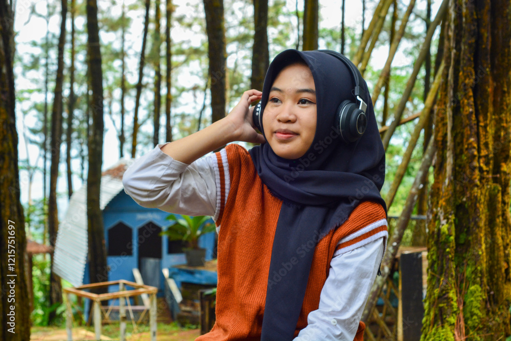 Naklejka premium Beautiful woman asian muslim standing in front of a fresh forest park with smart phone and headphones
