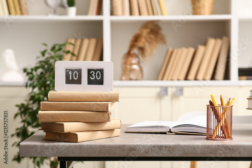 Modern flip clock displaying 10:30 AM on stack of books in home office settin...