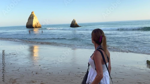 A Walk to Remember: Woman Captivated by the Sunset at the Beach of the Three Brothers (Praia dos Três Irmãos) in Algarve, Portugal.