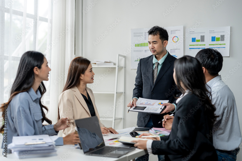 A group of people are gathered around a table with papers and laptops A group of people are gathered around a table with papers and laptops