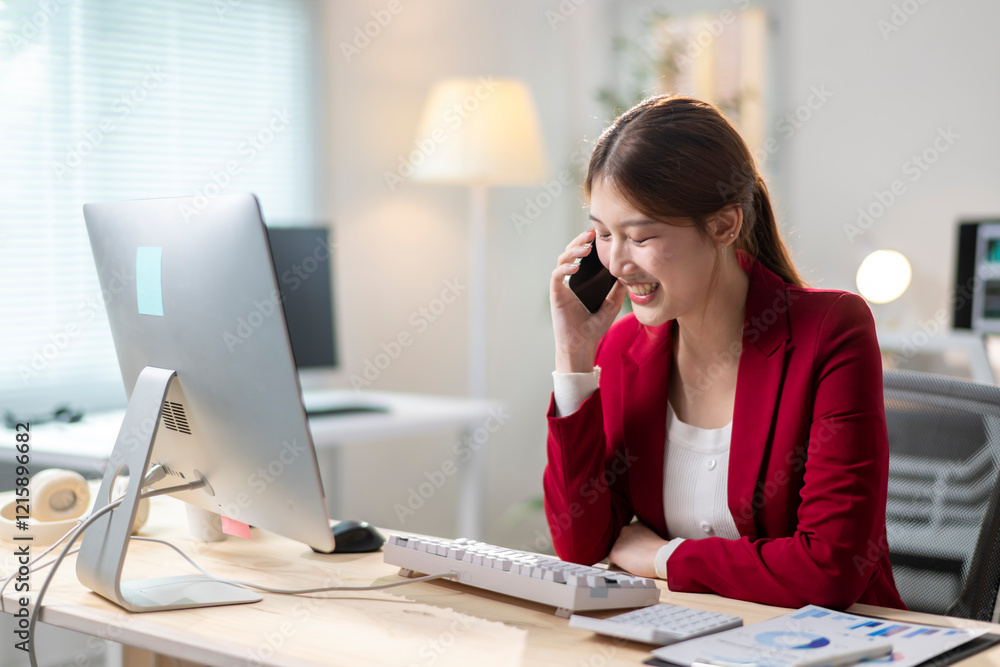 Obraz premium A woman in a red jacket is talking on her cell phone while sitting at a desk