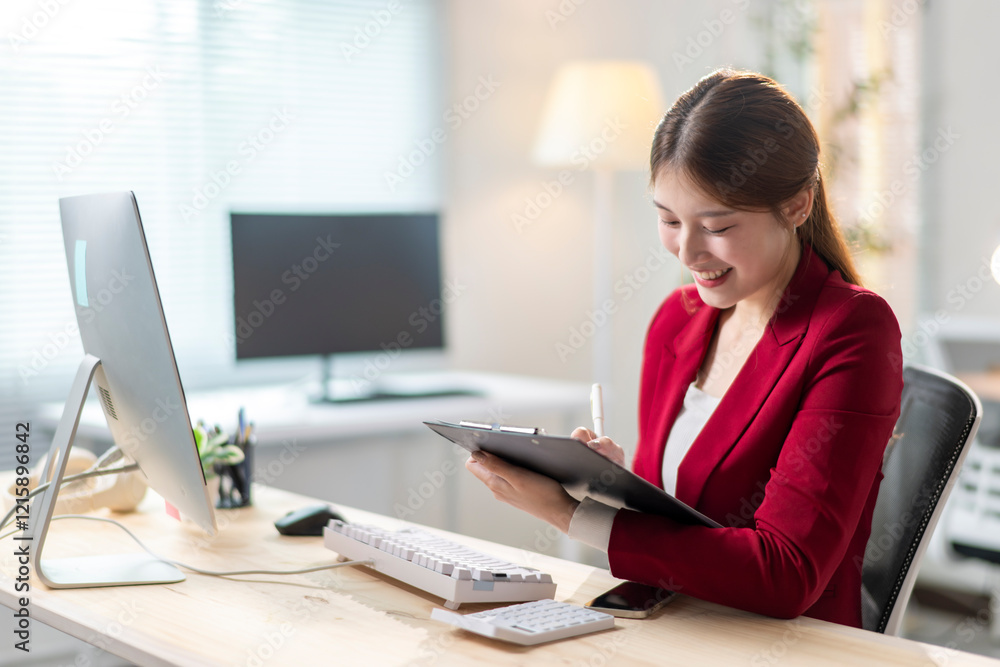 A woman in a red jacket is sitting at a desk with a clipboard in front of her A woman in a red jacket is sitting at a desk with a clipboard in front of her