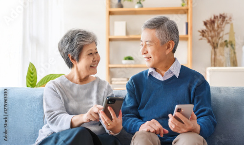 ソファーに座ってスマホの画面を見ている老夫婦（Elderly couple sitting on the sofa looking at a smartphone screen）
