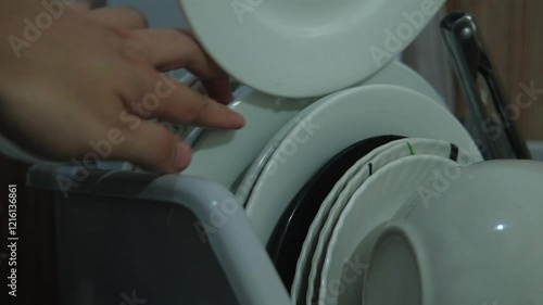 A white plate being placed in kitchen dishrack after washing. -static close-up shot photo