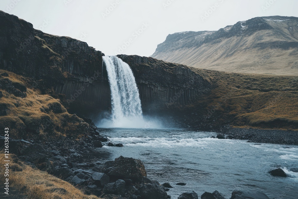 Majestic Waterfall cascading down volcanic cliffs into a clear river in Iceland Majestic Waterfall cascading down volcanic cliffs into a clear river in Iceland