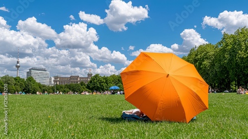 Fototapeta Naklejka Na Ścianę i Meble -  Person relaxing on green grass under a bright orange umbrella on a sunny day