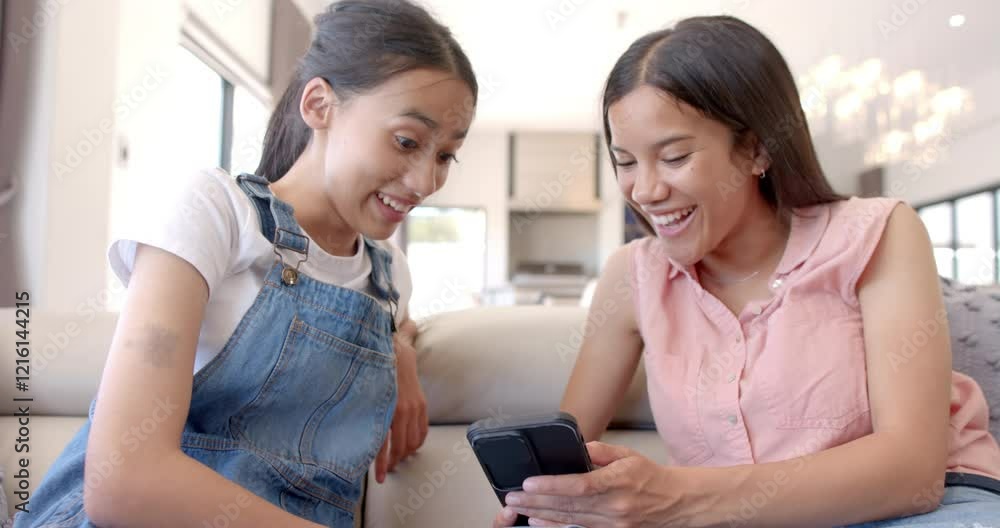 Teenage girls sitting on couch, smiling and looking at smartphone together Teenage girls sitting on couch, smiling and looking at smartphone together