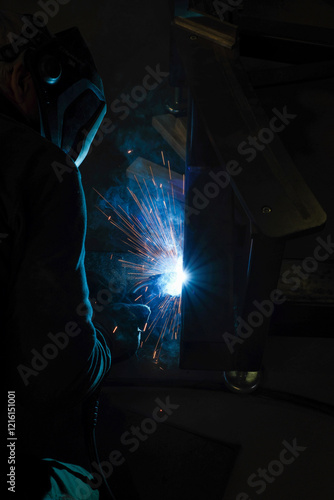 Obraz na płótnie a person wearing a welding mask works on metal with a welding torch, creating sparks through the welding process w salonie