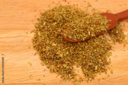 Dried oregano leaves or Origanum vulgare L. On a wooden spoon and some scattered around it, close up view.