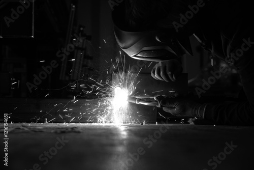Obraz na płótnie a person wearing a welding mask works on metal with a welding torch, creating sparks through the welding process w salonie