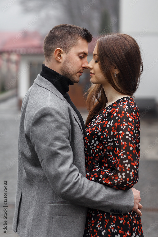 couple standing on the street. A man and a woman hug and touch each other's noses. The man is wearing a gray jacket and black turtleneck, and has short dark hair. couple standing on the street. A man and a woman hug and touch each other's noses. The man is wearing a gray jacket and black turtleneck, and has short dark hair.