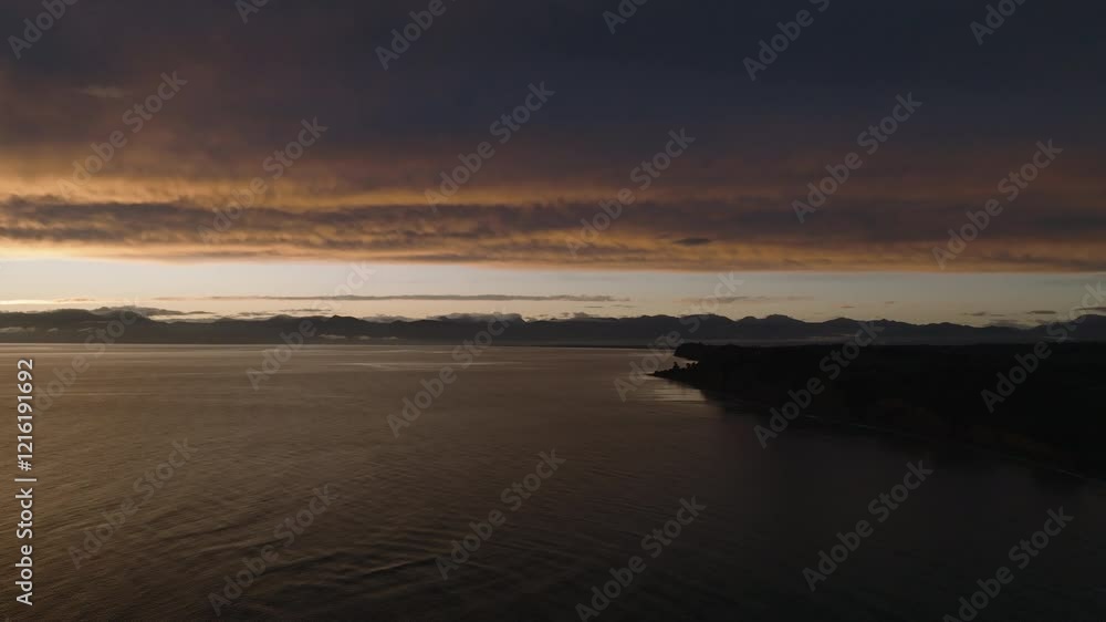 Drone Shot flying over the Tasman Coastline at Dusk with Silhouetted Land and Early Morning Glow Lighting Up the Mountains, New Zealand Drone Shot flying over the Tasman Coastline at Dusk with Silhouetted Land and Early Morning Glow Lighting Up the Mountains, New Zealand