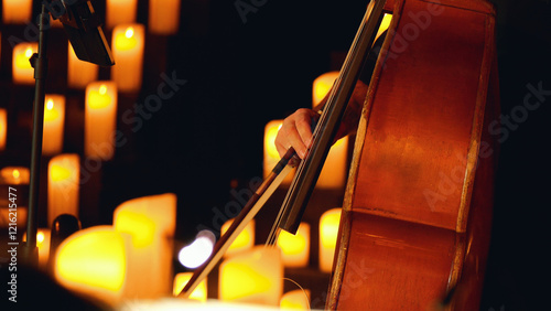 Close-up of a double bass being played on a stage with lit candles. The background is blurred and orange. Candlelight concert.