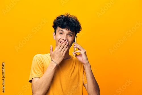 Canvastavla Young man smiling while talking on the phone, wearing a yellow t shirt against a