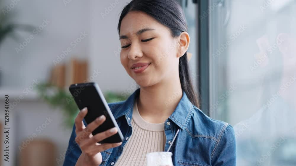 Video of cheerful woman eating yogurt while sending messages with smartphone in the living room at home. Video of cheerful woman eating yogurt while sending messages with smartphone in the living room at home.