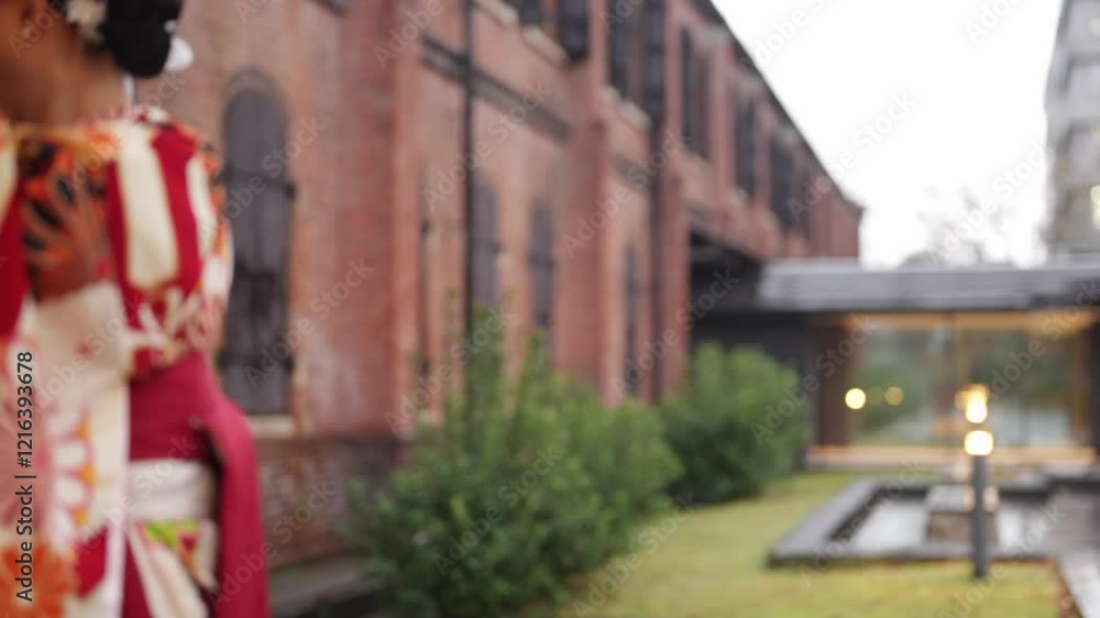 Young women in their 20s wear traditional hakama (kimono) in Japan, known for the graduation ceremony. She stands in the rain in front of a traditional brick, pointing to an umbrella. Young women in their 20s wear traditional hakama (kimono) in Japan, known for the graduation ceremony. She stands in the rain in front of a traditional brick, pointing to an umbrella.