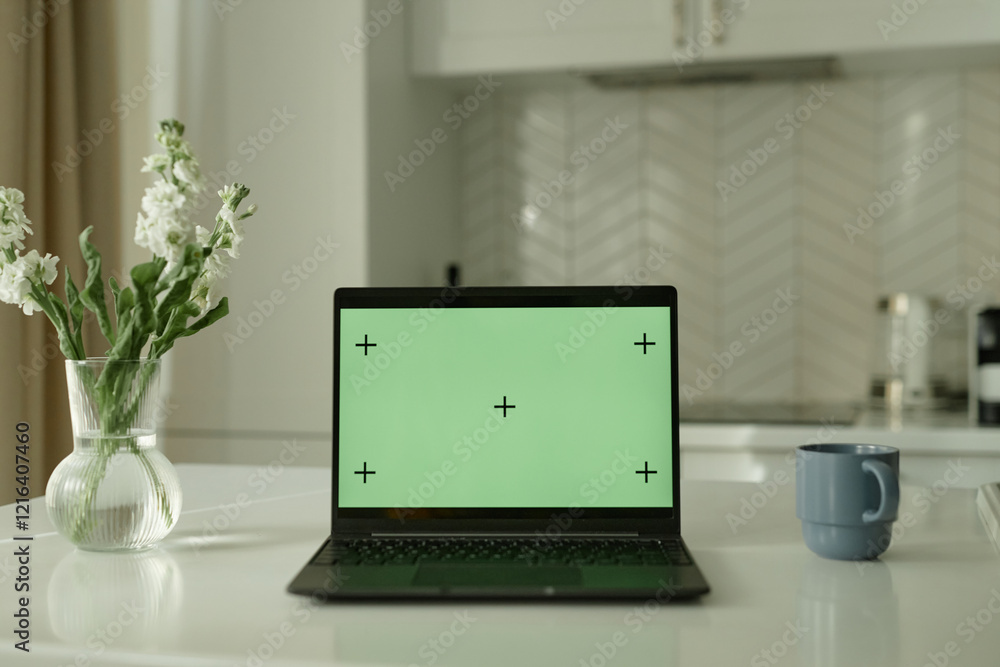 Background shot of open laptop with blank green mockup screen on counter in cozy white kitchen with minimalistic interior, copy space Background shot of open laptop with blank green mockup screen on counter in cozy white kitchen with minimalistic interior, copy space