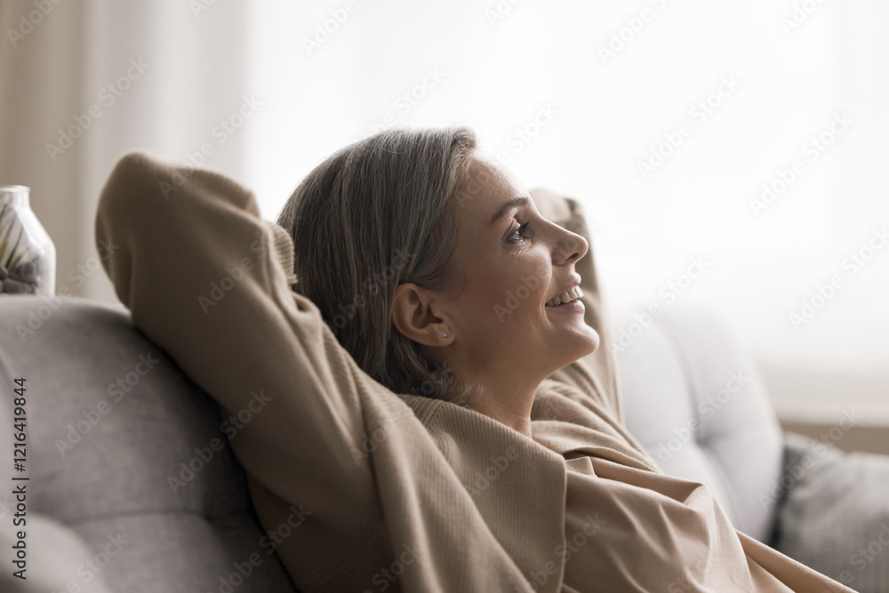 Personal time. Profile head shot portrait positive tranquil mature woman sitting on sofa with hands supporting head listen to calm peaceful music for relaxation reduce stress alone in cozy living room Personal time. Profile head shot portrait positive tranquil mature woman sitting on sofa with hands supporting head listen to calm peaceful music for relaxation reduce stress alone in cozy living room