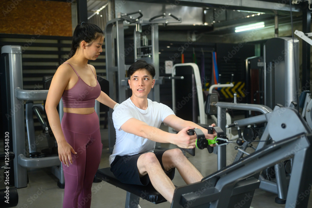Fototapeta premium Female coach supervising a male client working out on rowing machine in a modern gym