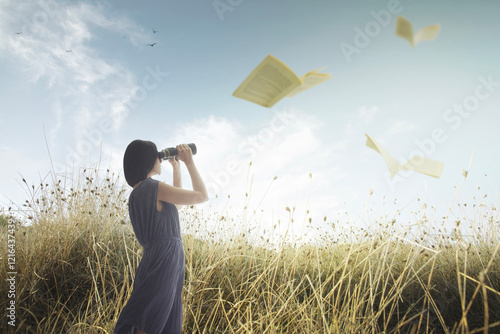 Woman with telescope watching pages of a book flying like birds in the middle of nature photo