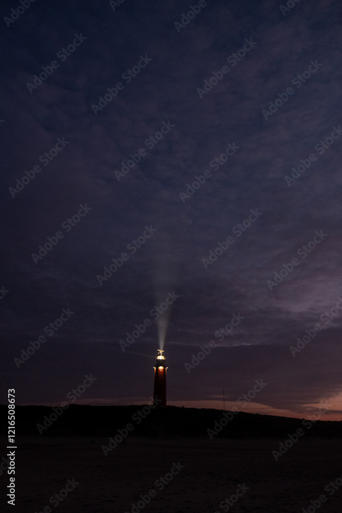 Obraz premium Eierland, De Cocksdorp, Texel, The Netherlands, Oktober 28th, 2024, A splendid lighthouse beams its bright light across the tranquil, dark sky at dusk, signifying guidance and safety