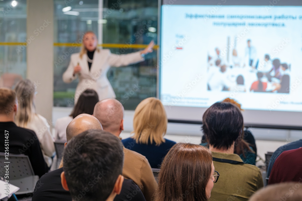 Fototapeta premium Corporate seminar session with a presenter addressing an engaged audience in a modern venue. Attendees focused on the speaker delivering a presentation.