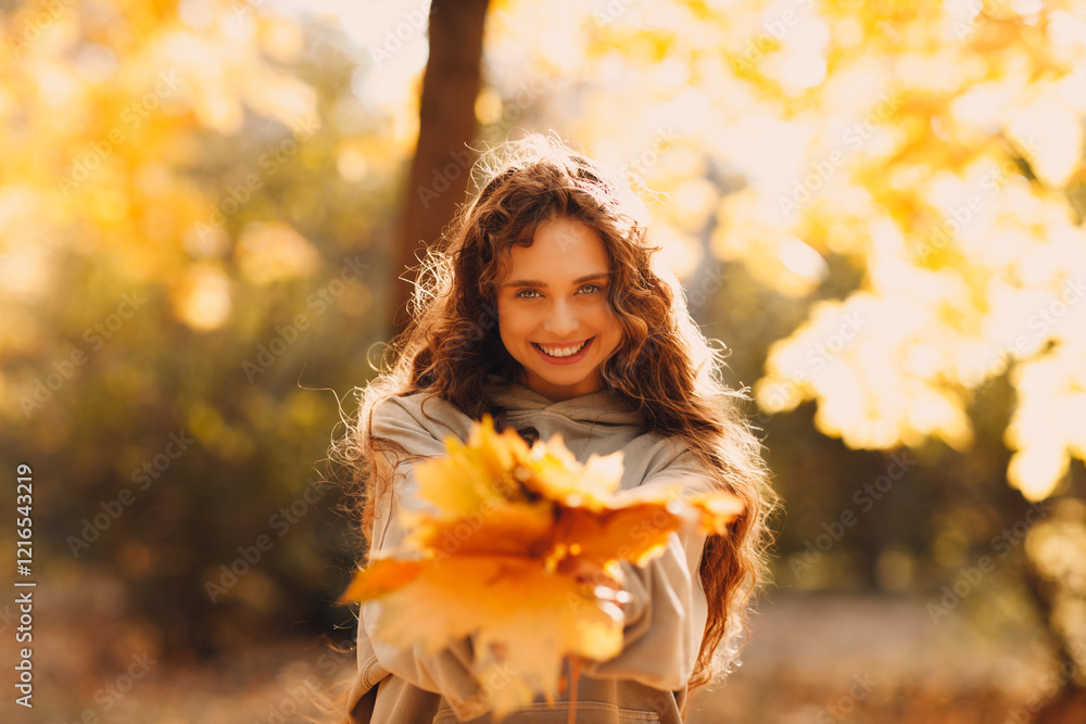 Smiling young woman enjoys the autumn weather in the fall park with the yellow leaves at sunset Smiling young woman enjoys the autumn weather in the fall park with the yellow leaves at sunset