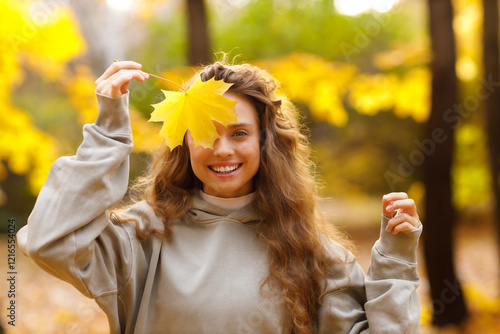 Obraz na płótnie Young woman holds yellow leaf in her hand with smile in the park at sunset w salonie
