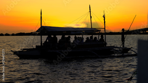 A silhouette of a traditional Philippine boat carrying passengers, gliding over tranquil waters beneath a vibrant sunset, evoking a serene and scenic atmosphere.