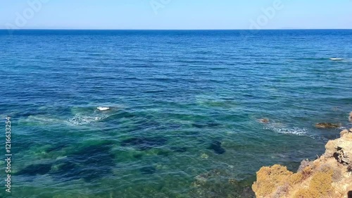 A blue sea with waves and a rocky coastline.