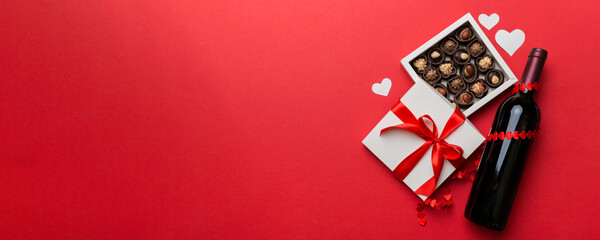 Bottle of red wine on colored background for Valentine Day with gift and chocolate. Heart shaped with gift box of chocolates top view with copy space