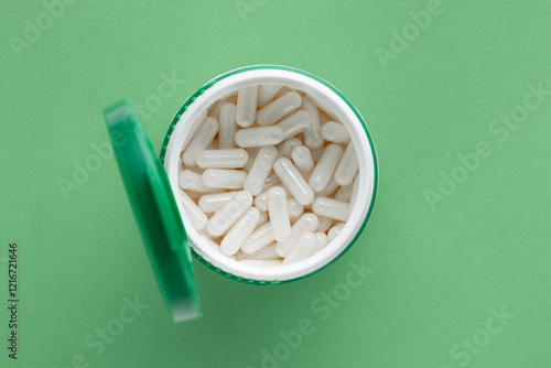 White plastic bottle of white capsules and green lid. Medical concept for the treatment of diseases with drugs. Vitamins, pills for every day or antibiotics. Top view on green background photo