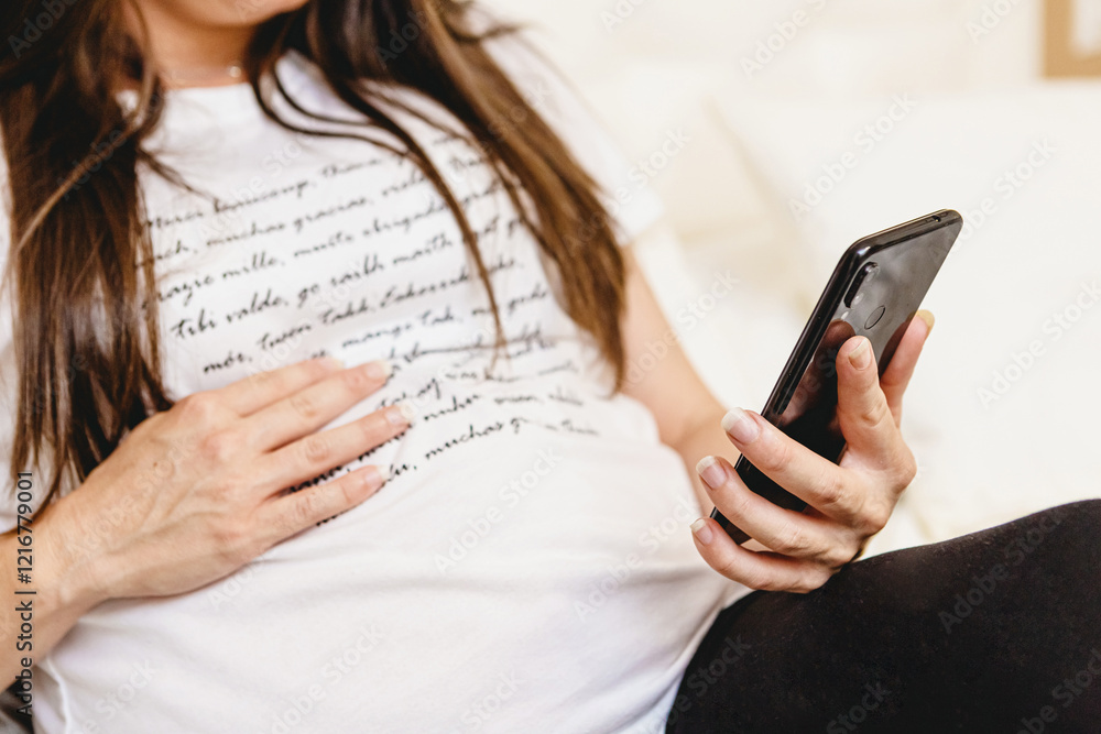 Closeup of pregnant woman using a mobile phone while resting on bed Closeup of pregnant woman using a mobile phone while resting on bed