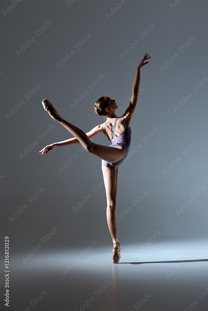 Fototapeta premium Professional ballerina in lavender leotard performing an elegant arabesque on pointe in studio lighting.