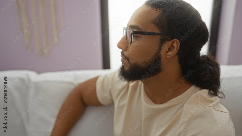 Fototapeta premium Young man with beard relaxing indoors in a comfortable living room setting with natural light.
