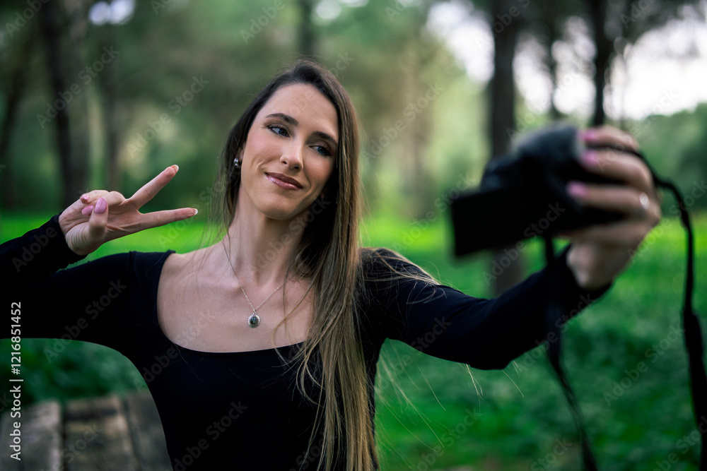 Chica joven delgada vloggeando con cámara por zona verde con arboles