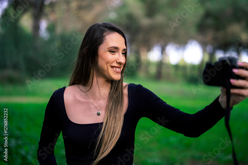 Obraz na płótnie Chica joven delgada vloggeando con cámara por zona verde con arboles w salonie